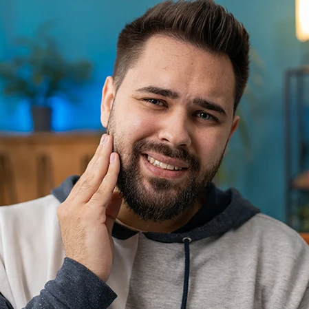 young man with small beard is touching his jaw wincing in pain